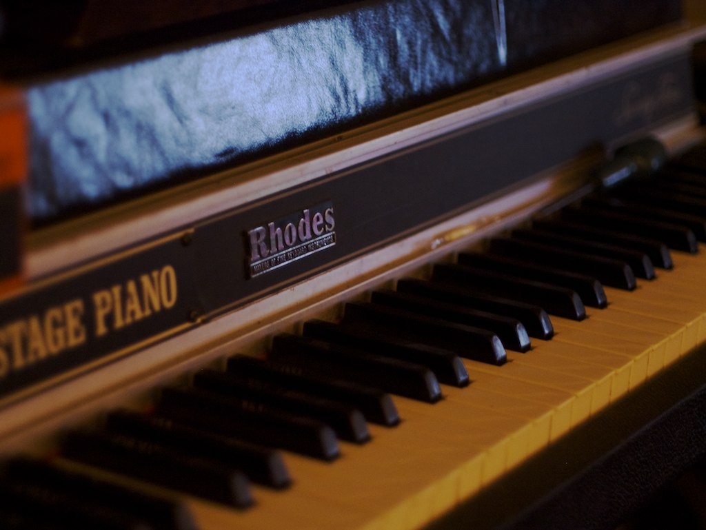 A Fender Rhodes Stage piano — the "Rhodes" badge and "STAGE PIANO" name rail above the wood-grain keys identify a passive Stage instrument, which carries no speaker cabinet beneath it. Reference im…
