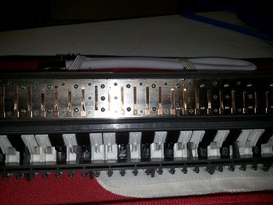 Figure 3 — A melodica free-reed plate being scratched to retune the tongue: scratching the tip raises pitch, the middle lowers it. The exact free-reed recipe is Vol 05.